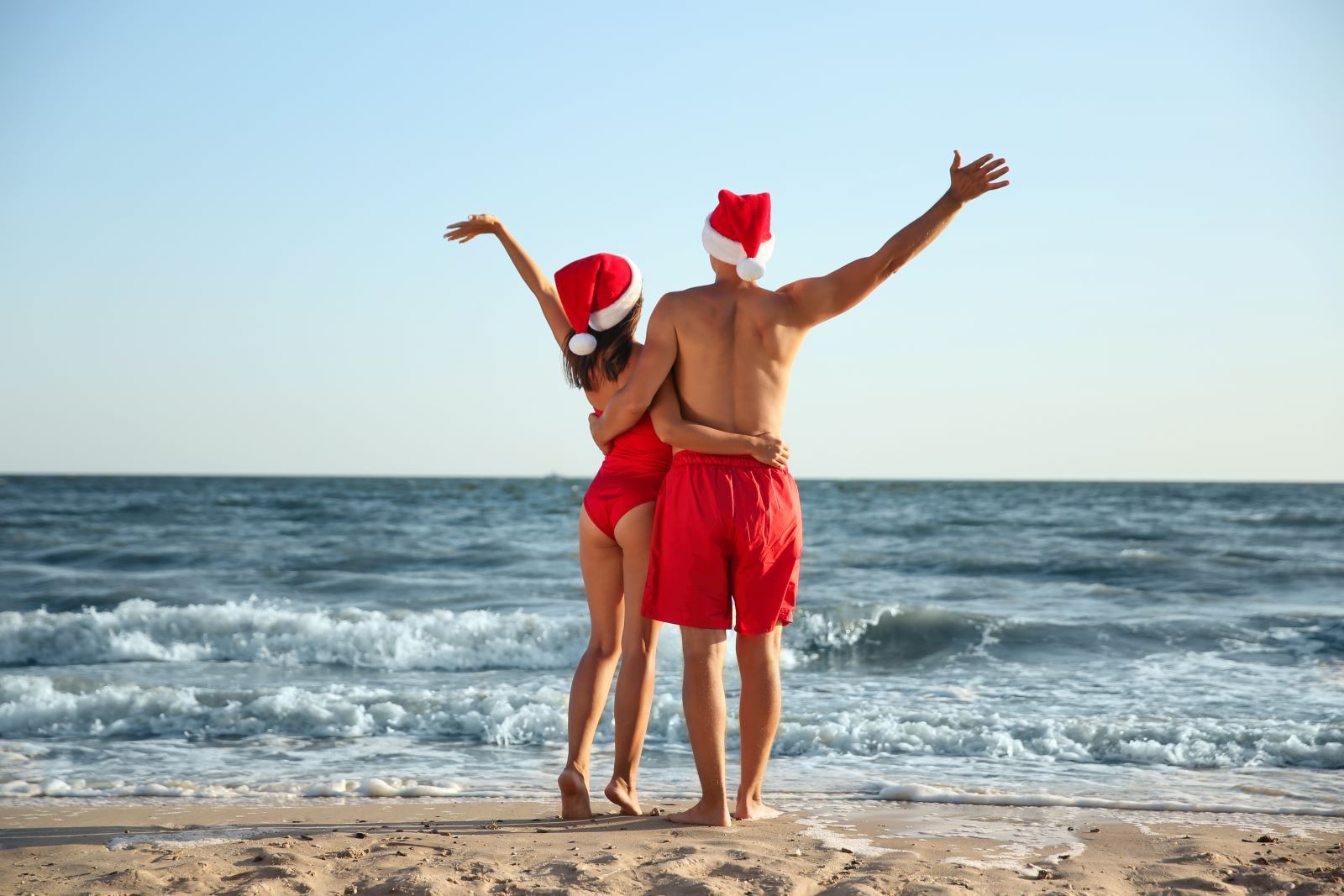 two people wearing santa hats on the beach